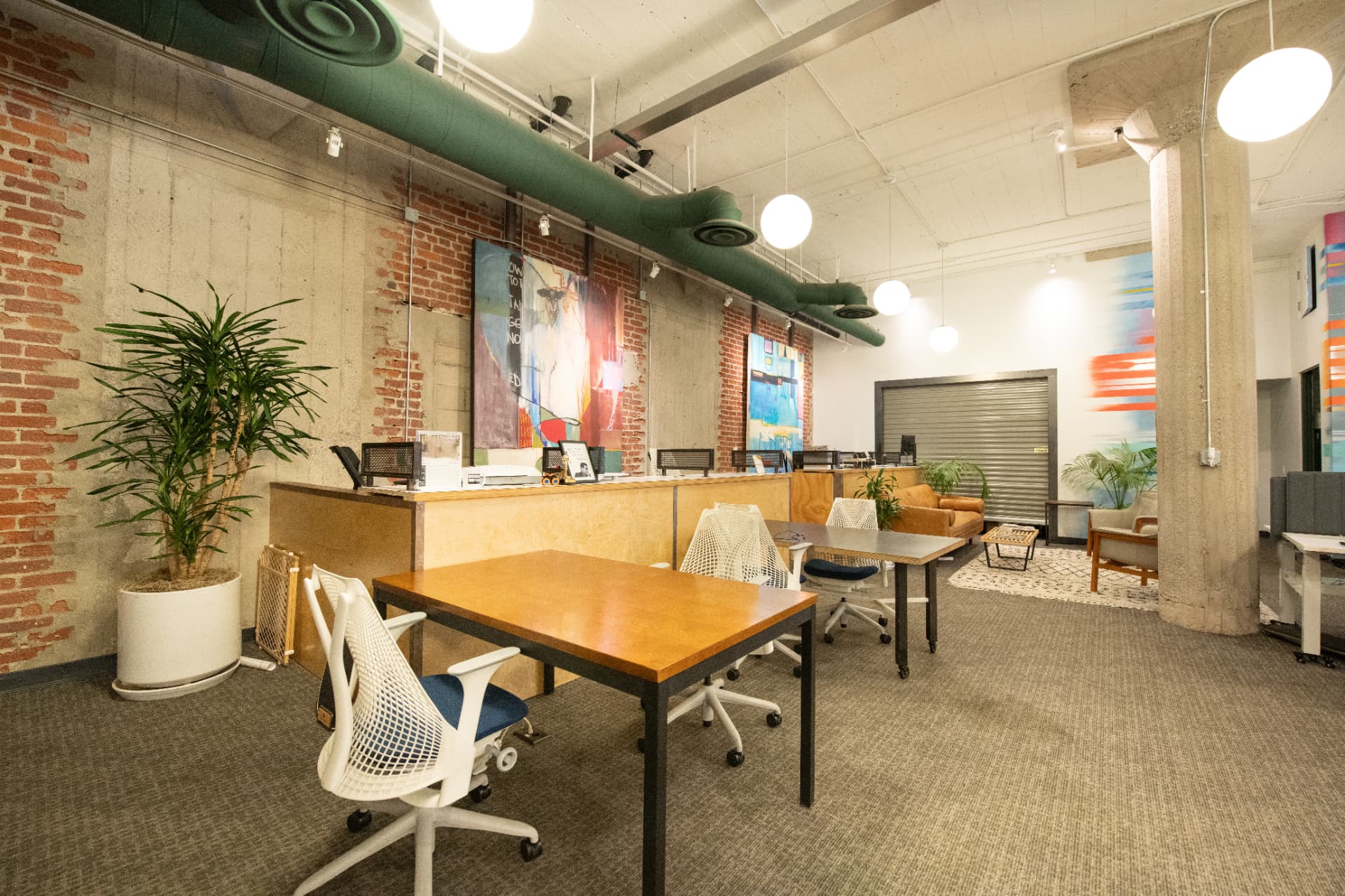 Dedicated desk area at Kiva Funk Zone with wood desks, ergonomic chairs, exposed brick walls and abstract artwork