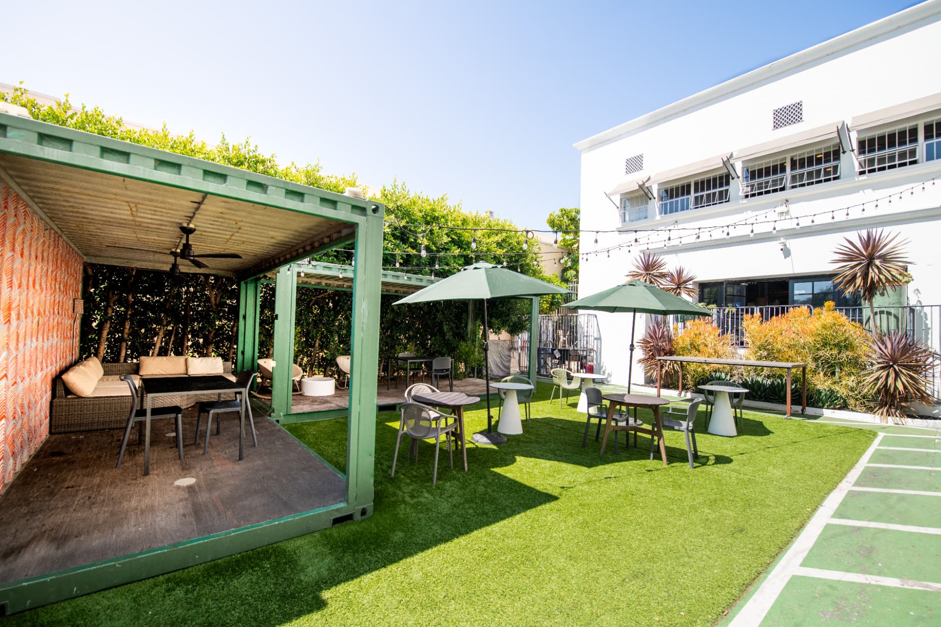 Outdoor courtyard at Kiva State St. with shaded cabanas, café tables and a turf lawn