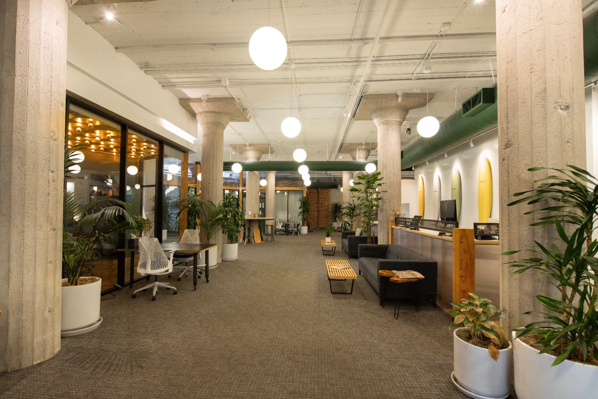 Central hallway at Kiva Funk Zone with concrete pillars, globe pendant lighting, a lounge sofa and wall-mounted surfboards